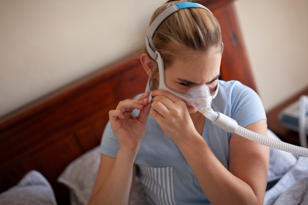 Woman adjusting CPAP mask for sleep apnea treatment in bedroom setting, highlighting oral appliance therapy alternatives.