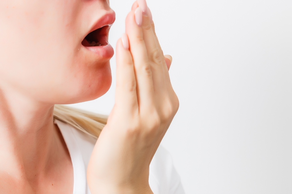 Woman covering mouth while exhaling, illustrating concerns about bad breath in dental health context.