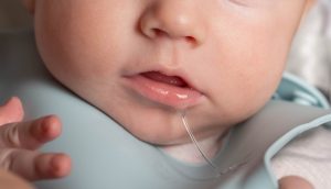 Close-up of a baby with saliva dripping from their mouth, wearing a blue bib, emphasizing the importance of saliva in oral health.