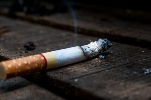 Cigarette resting on wooden surface, with smoke rising, emphasizing the health risks associated with smoking and dry mouth.