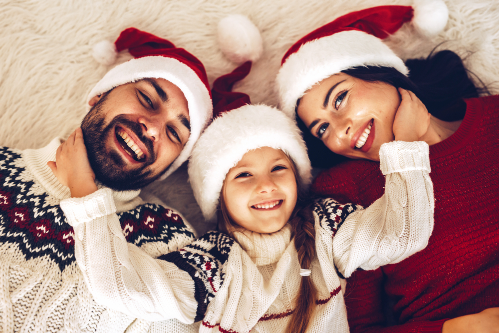 Family wearing festive sweaters and Santa hats, smiling together, promoting joyful holiday moments and confident smiles.